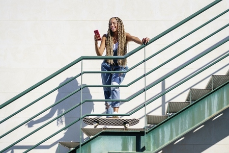 Black female with coloured braids looking at her smartphone with her feet resting on a skateboard