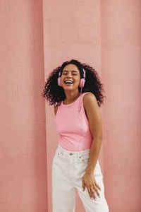 Young happy woman in casuals wearing pink headphones listening music with closed eyes