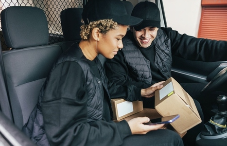 Two couriers sitting in van checking information on box for delivery