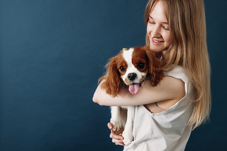 Young smiling pet owner holding her cute little dog in studio against a blue background