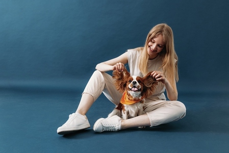 Smiling woman sitting on blue background and playing with her dog
