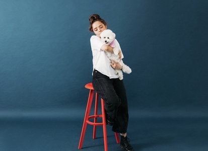 Woman in casuals sitting on chair in studio with her little fluffy dog