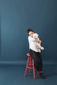 Pet parent hugging her little fluffy dog while sitting on chair in studio