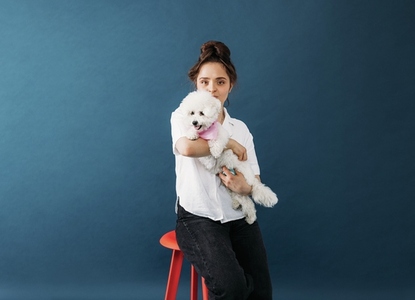 Young woman hugging her little white dog in studio while sitting on chair