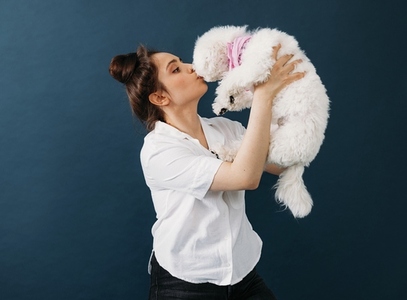 Side view of a woman holding and kissing her little white dog in studio