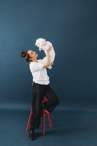 Side view of pet owner lifts up her little white dog against blue background
