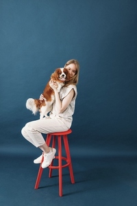 Young pet owner sitting on a red chair in studio holding a little dog on hands