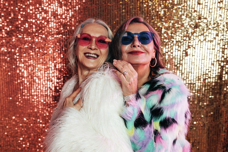 Two smiling senior women in fur coats posing together in studio