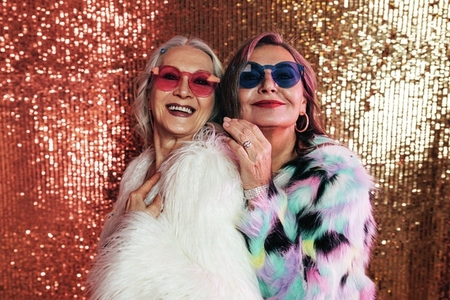 Two smiling senior women in fur coats posing together in studio