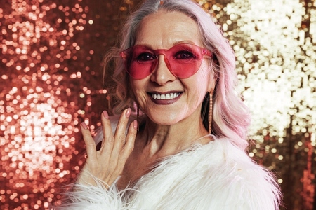 Close up of a smiling senior woman with grey hair wearing pink eyeglasses looking at camera