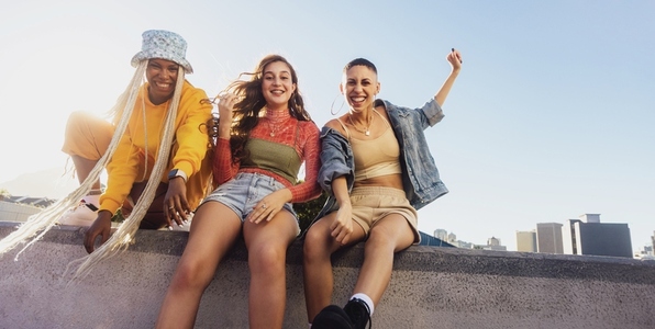 Three female friends smiling while sitting on a wall