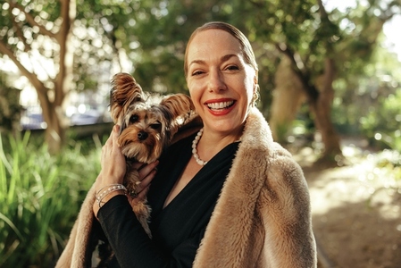 Happy posh woman smiling at the camera while holding her dog