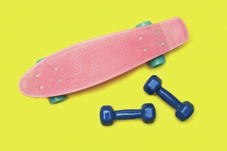 Skateboard and dumbbells on yellow background