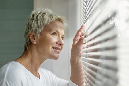 Smiling woman looking through window blinds
