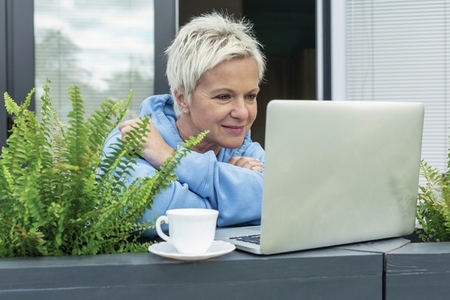 Woman with tea working at laptop on patio