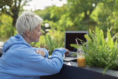 Woman with juice working at laptop on patio