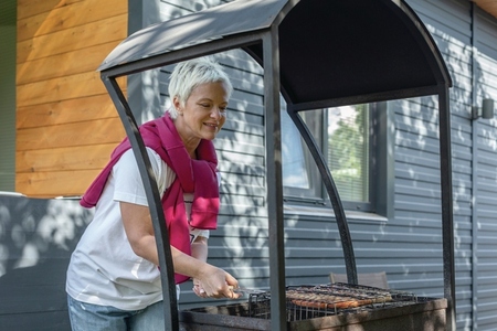 Woman grilling sausages at patio barbecue