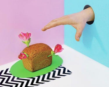 Hand in hole reaching for mini loaf of bread with flowers