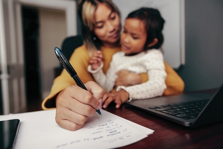 Working mom writing notes while holding her daughter