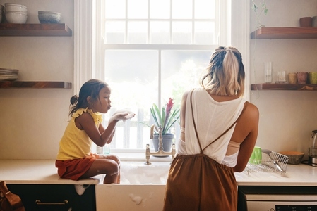 Young girl blowing soap bubbles at her mom in the kitchen