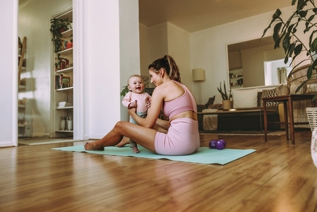 Young mother holding her adorable baby on an exercise mat