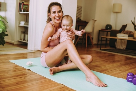 Smiling mom holding her baby while sitting on an exercise mat