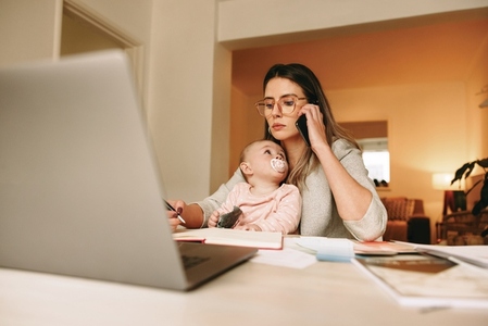 Young mom writing notes during a phone call in her home office
