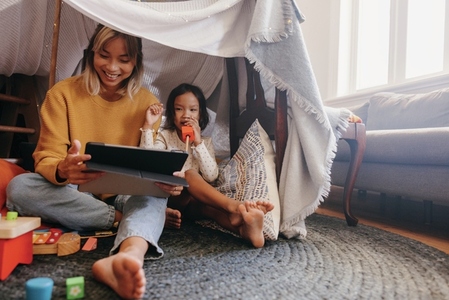 Cheerful mother and daughter watching kids content on a tablet