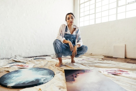 Female painter squatting in the middle of her paintings