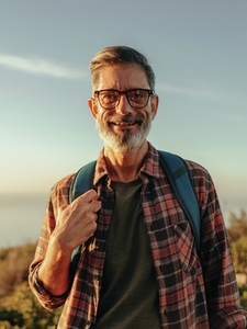 Cheerful mature hiker smiling at the camera while standing on a hilltop