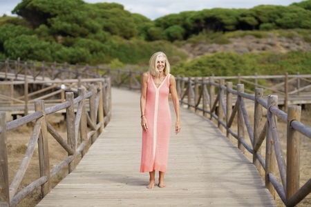 Beautiful mature woman walking along a wooden path near the beach   wearing a nice orange dress