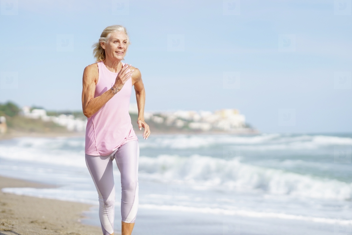Mature woman running along the shore of the beach. Older female doing sport to keep fit