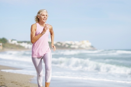 Mature woman running along the shore of the beach Older female doing sport to keep fit