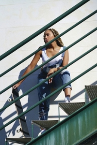 Young black woman with afro braids on an urban staircase  carrying a skateboard