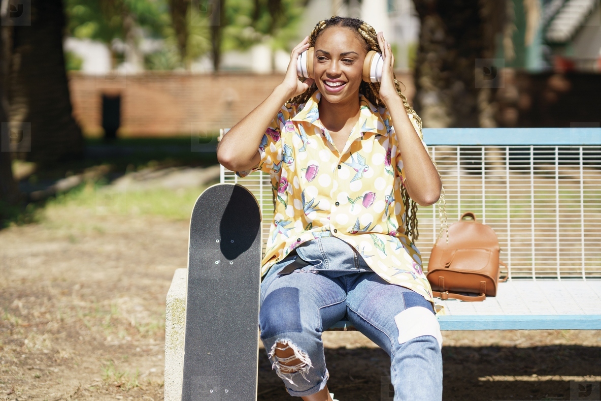 African woman with skateboard relaxing after riding skateboard listening to the music