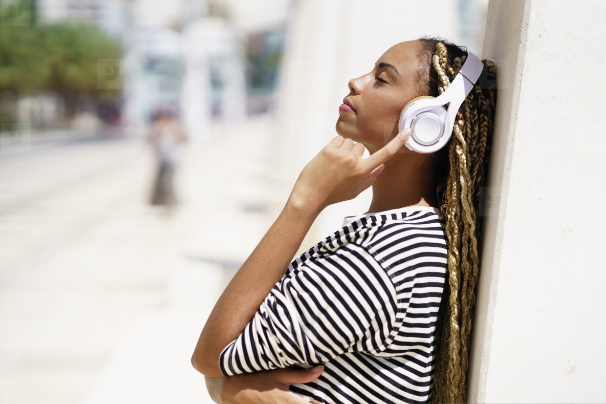 Young black woman listening to music with wireless headphones outdoors