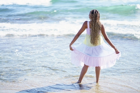 Black girl walking along the shore of the beach wearing a beautiful long dress