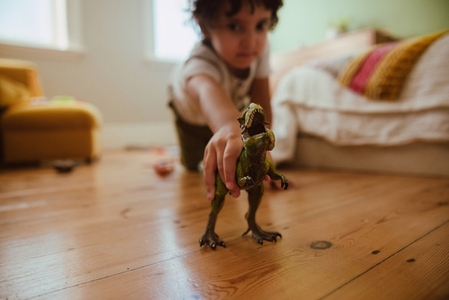 Ethnic boy playing with a t rex dinosaur at home