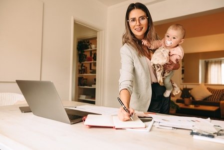 Creative businesswoman writing notes while holding her baby