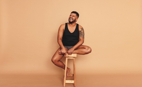 Tattooed man sitting on a wooden chair in a studio