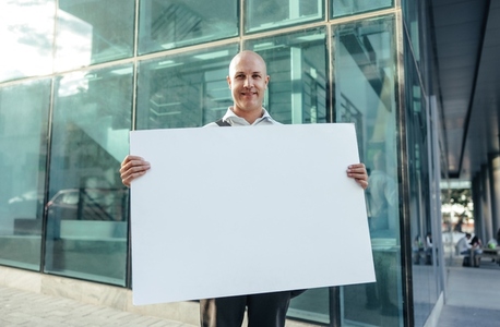 Cheerful businessman holding a blank banner outside his workplace