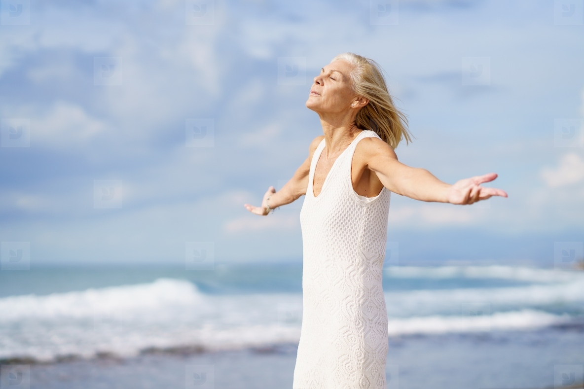 Mature woman breathing the beach air with her eyes closed and her arms open