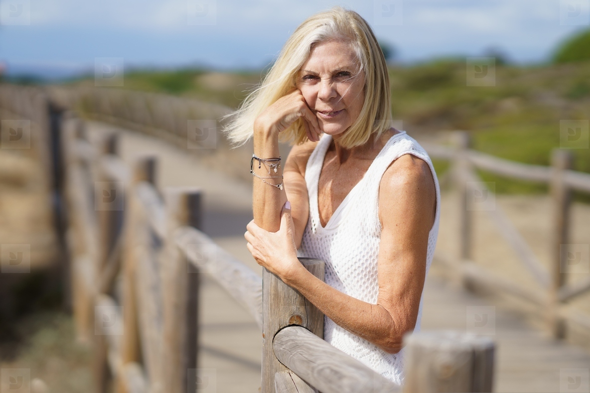 Happy female in her 60s leaning on wooden fences on the sand of a tropical beach