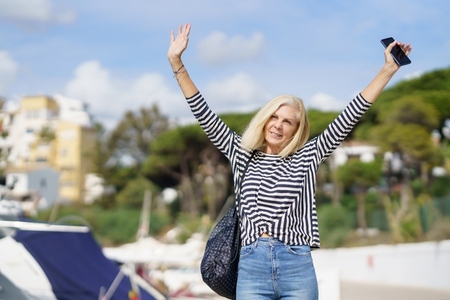 Woman in her 60s strolling along a seaside spot near the beach  raising her arms in joy