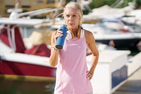 Senior woman in fitness clothing drinking water from a metal fitness bottle outdoors
