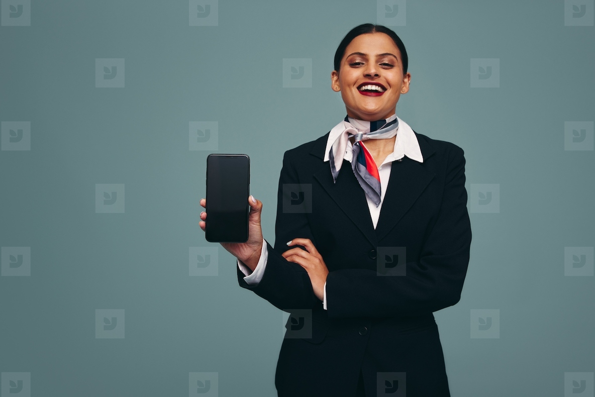 Young flight attendant holding up a smartphone in a studio
