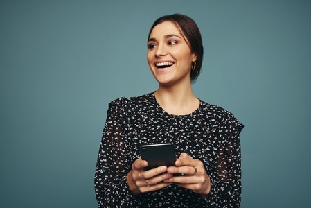Happy young woman holding a smartphone in a studio