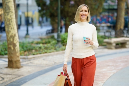 Woman shopping and carrying shopping bags and a coffee in a to go cup