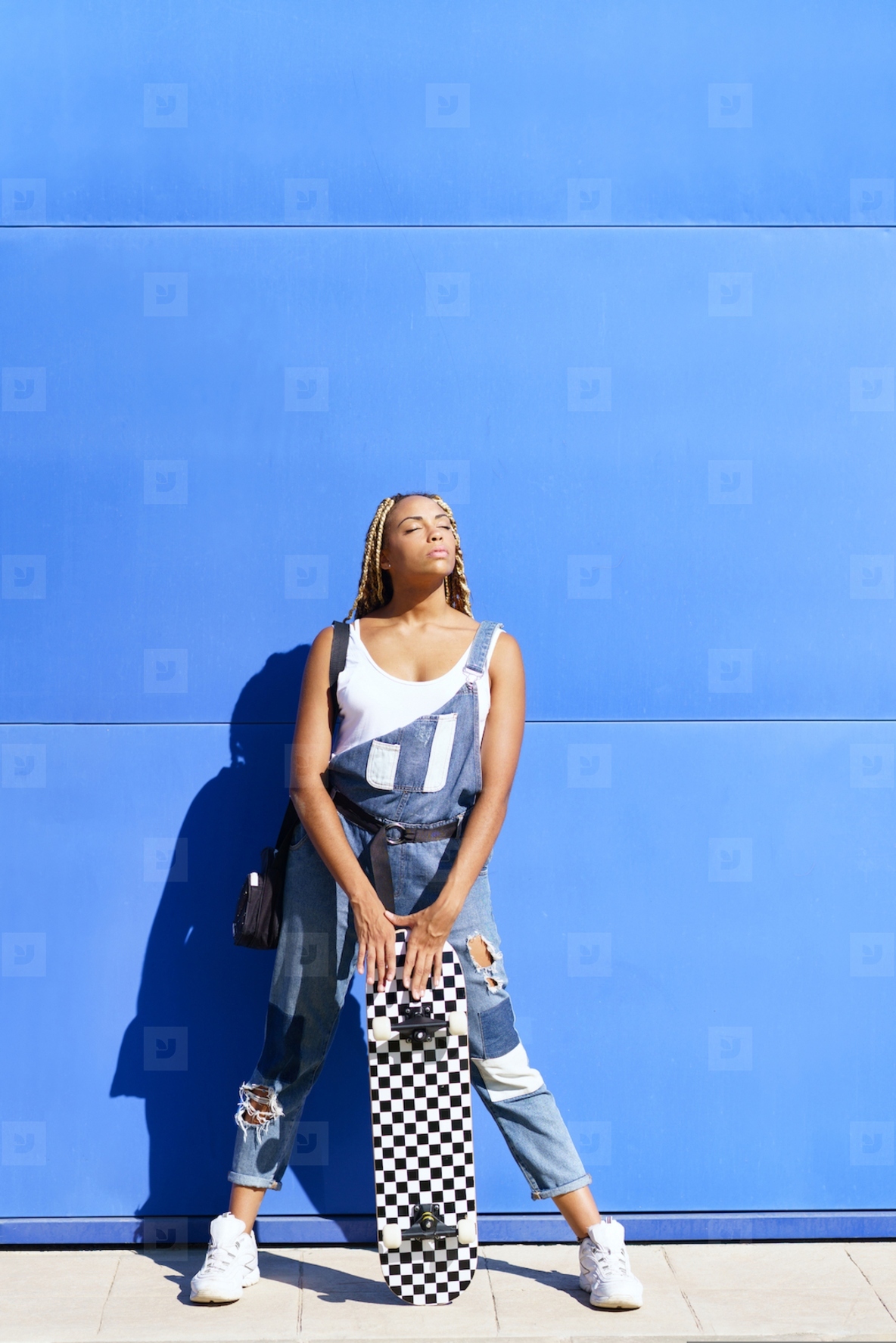 Black girl dressed casual  wtih a skateboard on blue wall background