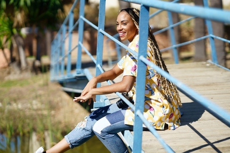 African girl combed with braids sitting on an urban bridge with a camera on vacation